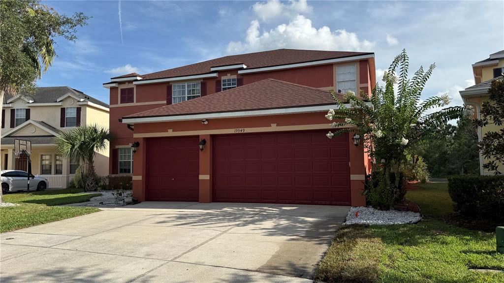 A two-story house with a red exterior and a three-car garage under a cloudy sky — 19949 TAMIAMI AVENUE, TAMPA, FL