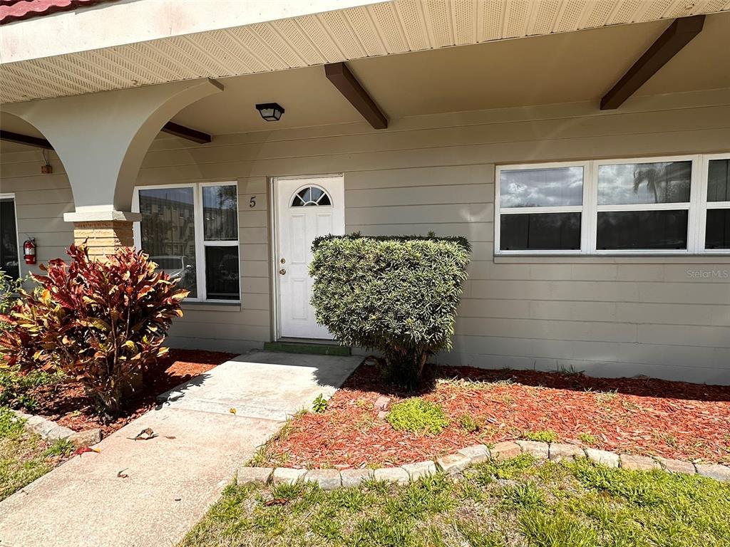 The exterior of a single-story building features a white front door, windows, and landscaping — 2073 DENMARK STREET UNIT 5, CLEARWATER, FL