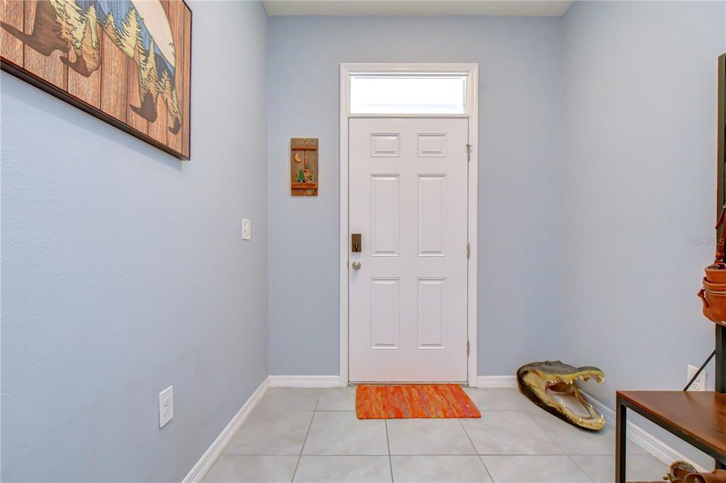An entryway with light blue walls, tile flooring, a white front door, and alligator decor — 3143 PLEASANT WILLOW COURT, BRANDON, FL