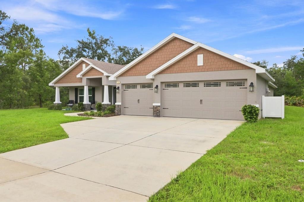 A single-story house with a three-car garage, tan stucco siding, and a brown shingled roof — 14 LUPINE STREET, HOMOSASSA, FL