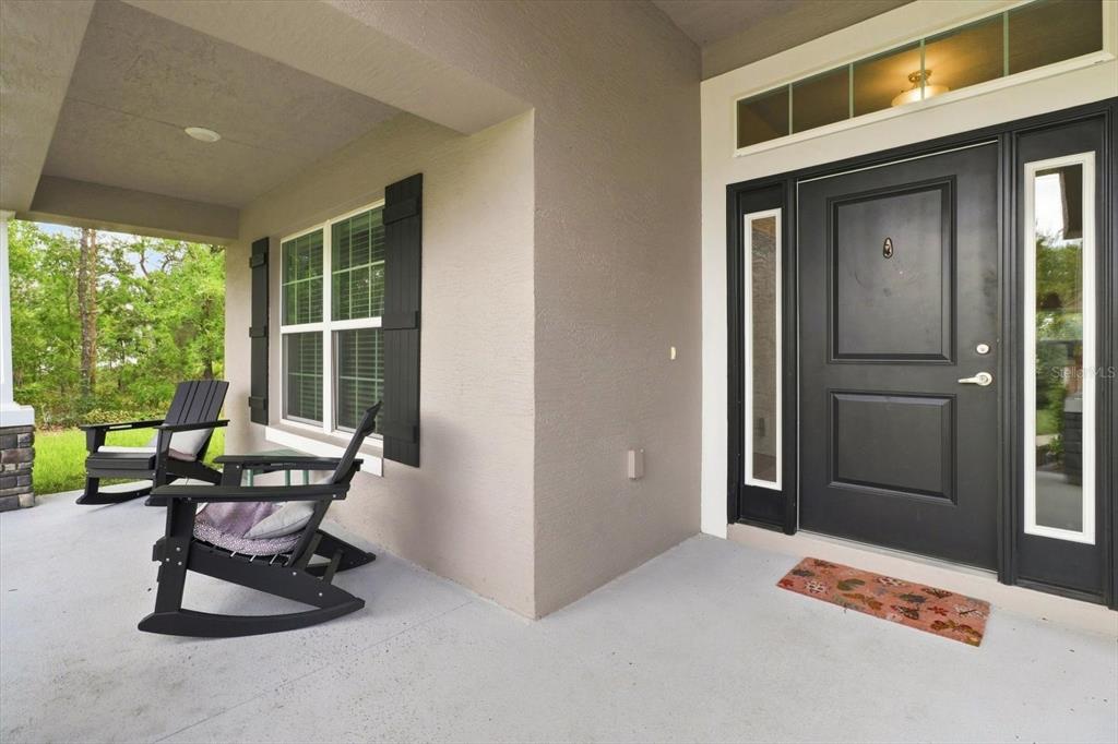 A covered front porch features two black rocking chairs, a dark door, and a doormat — 14 LUPINE STREET, HOMOSASSA, FL