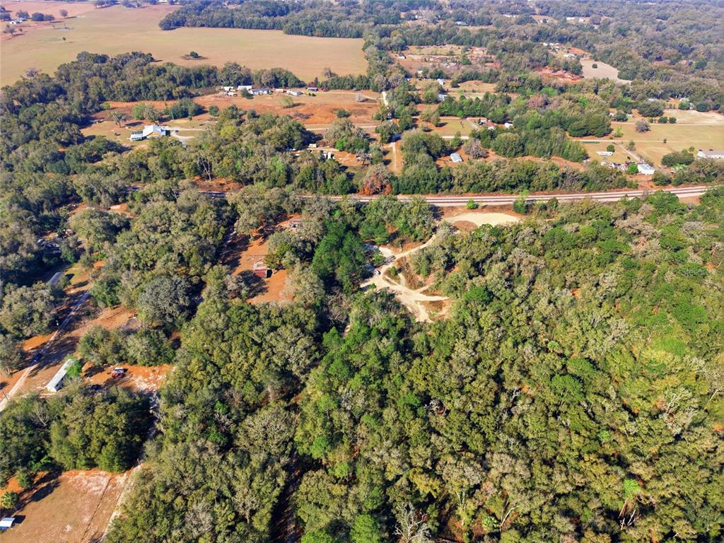 An aerial view shows a rural property with dense trees, dirt paths, and nearby railroad tracks — LOT 028 NE 164TH LANE, CITRA, FL