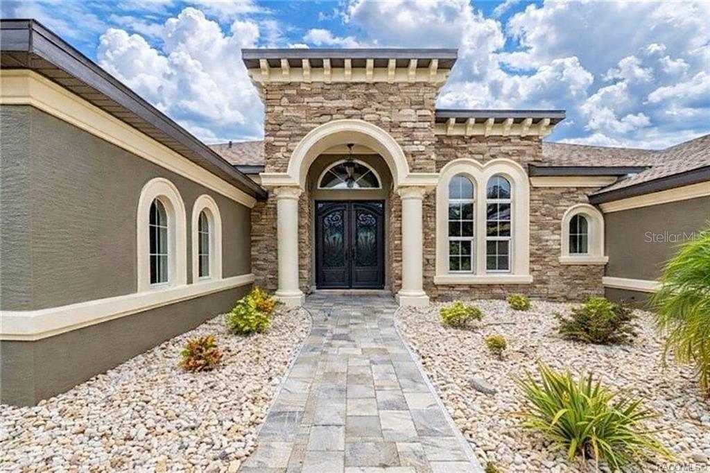 The exterior of a house features a stone facade, arched windows, and a paved walkway — 5061 W OAKHILL STREET, DUNNELLON, FL
