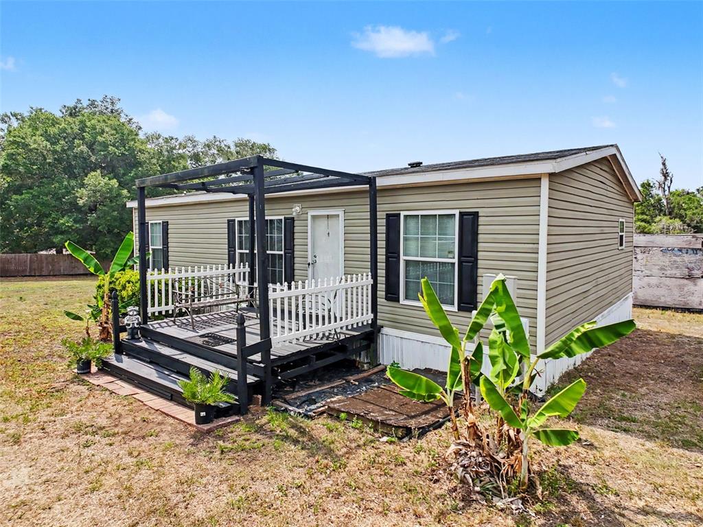 A single-story manufactured home with tan siding, black shutters, and a wooden deck with pergola — 28402 SOARING HAWK LANE, BROOKSVILLE, FL