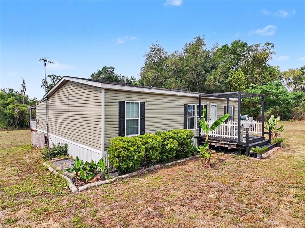 A single-story manufactured home with light green siding, a wooden deck, and landscaping — 28402 SOARING HAWK LANE, BROOKSVILLE, FL