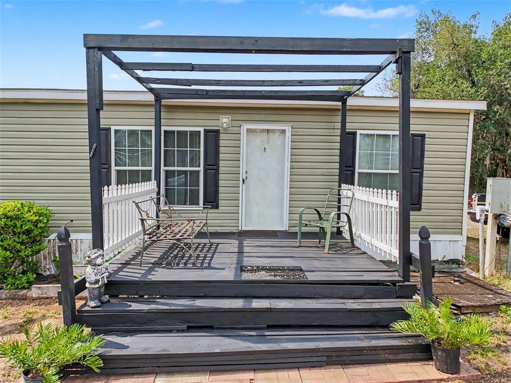 A mobile home exterior features a dark wooden deck with a pergola and white fencing — 28402 SOARING HAWK LANE, BROOKSVILLE, FL