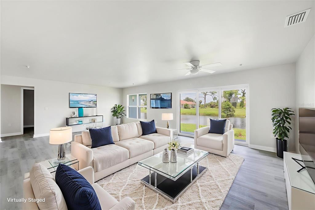 A virtually staged living room features light flooring, a white sofa set, and sliding glass doors — 236 BOUNDARY BOULEVARD, ROTONDA WEST, FL