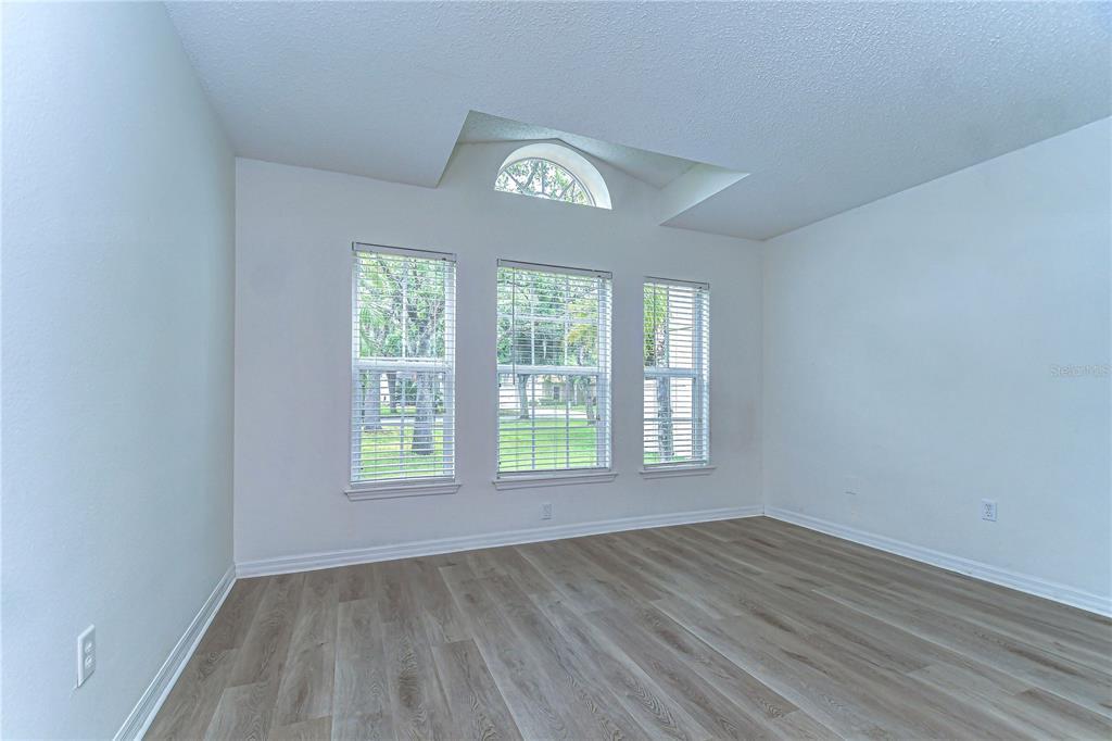 An empty room features light wood-look flooring, white walls, and three windows with blinds — 18303 ELMHURST LANE, TAMPA, FL