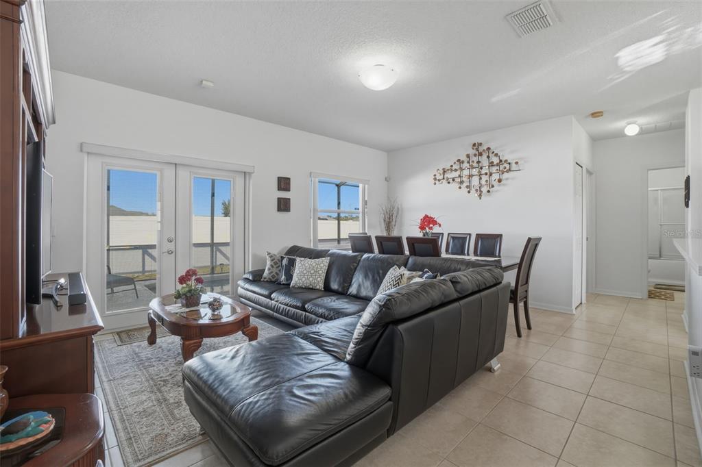 A living room with a black sectional sofa, dining area, and sliding glass doors to outside — 995 CUMBERLAND DRIVE, KISSIMMEE, FL