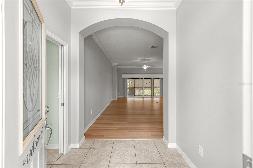 An entryway with tiled floors leads into a living area featuring hardwood flooring and arches — 2875 ADRIENNE WAY, THE VILLAGES, FL