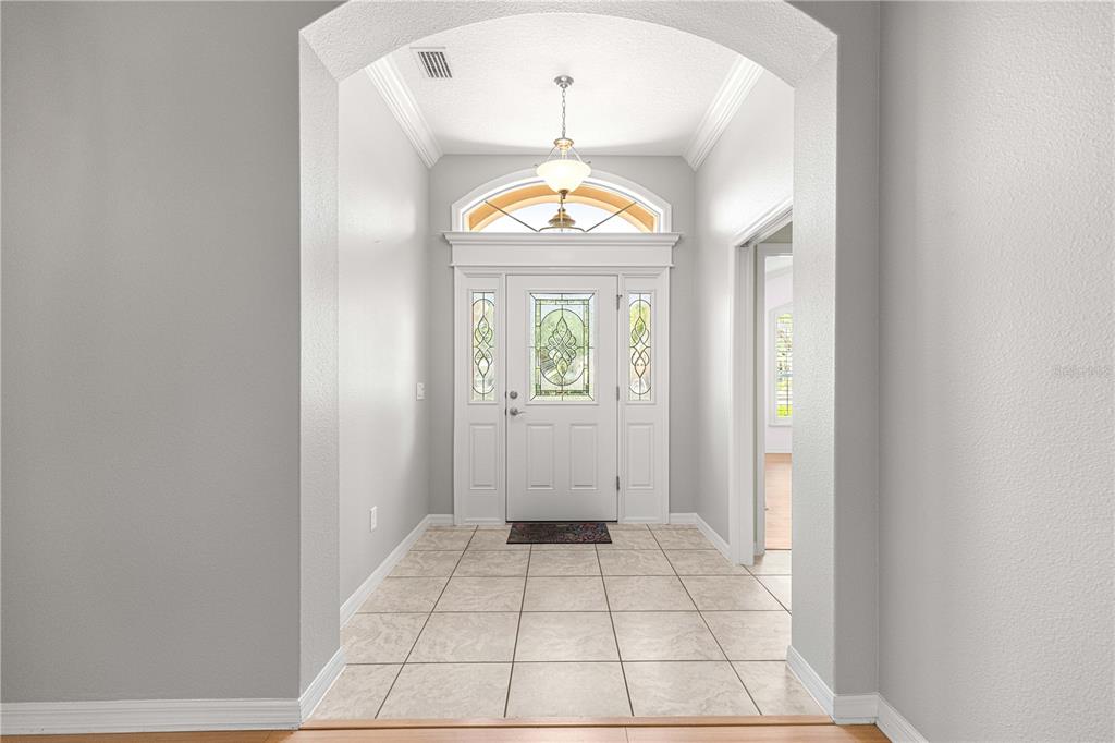 A bright entryway features a white front door with glass panels and tiled flooring — 2875 ADRIENNE WAY, THE VILLAGES, FL