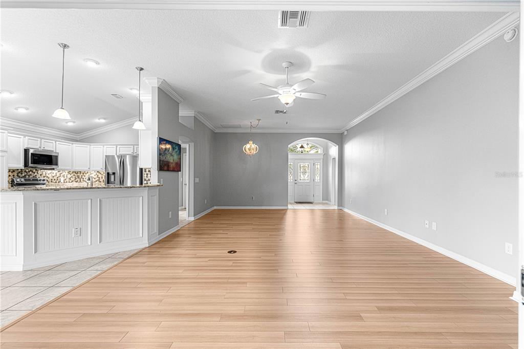 An open-concept living and dining area features light wood flooring, white cabinetry, and a ceiling fan — 2875 ADRIENNE WAY, THE VILLAGES, FL