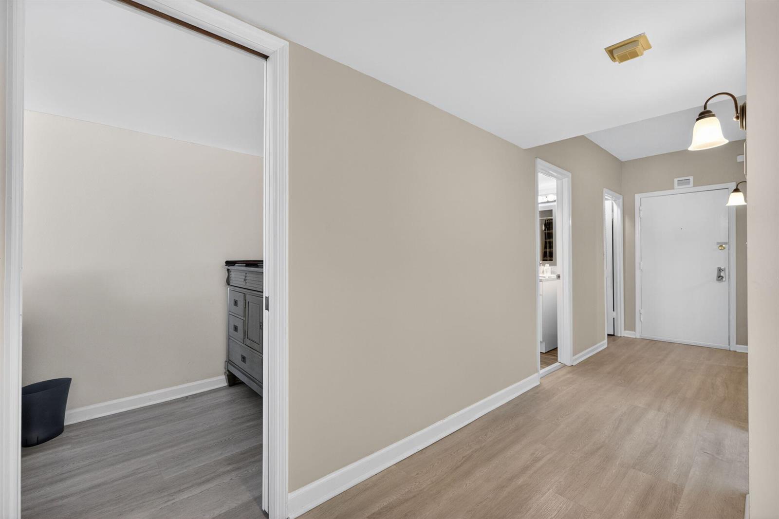 A hallway with light wood-look flooring leads to an entryway door and two doorways — 1200 Marine Way, North Palm Beach FL 33408, NORTH PALM BEACH, FL