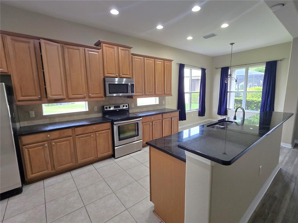 A kitchen features wood cabinets, black countertops, stainless steel appliances, and tile flooring — 3637 SUMMERWIND CIRCLE, BRADENTON, FL