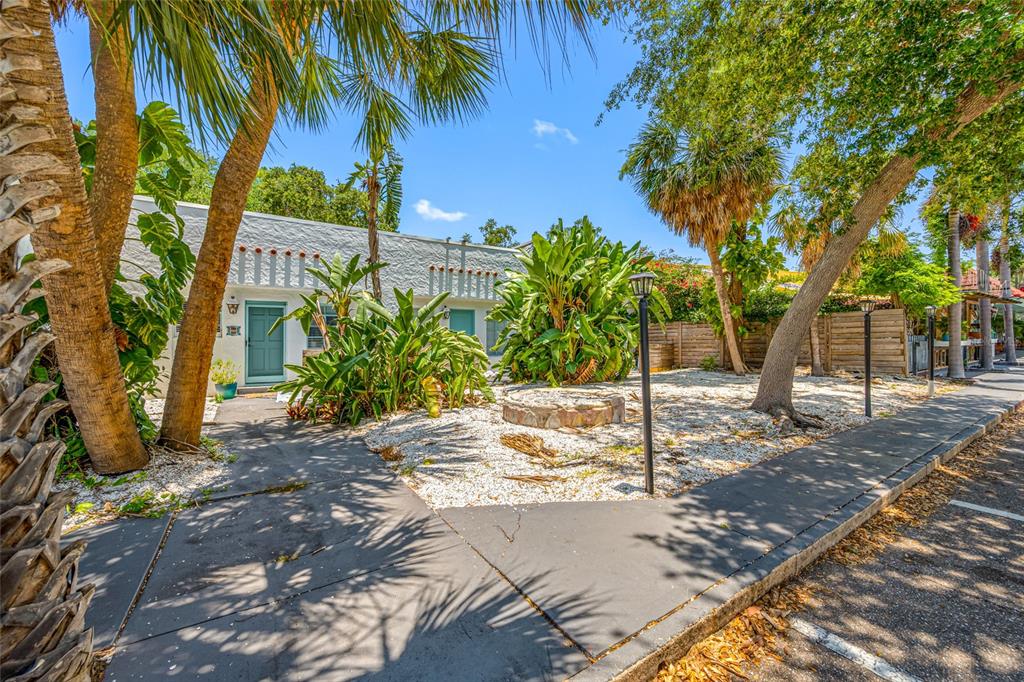 A single-story white building with a teal door sits behind a gravel yard and palms — 1700 PARK STREET N UNIT 105, ST PETERSBURG, FL