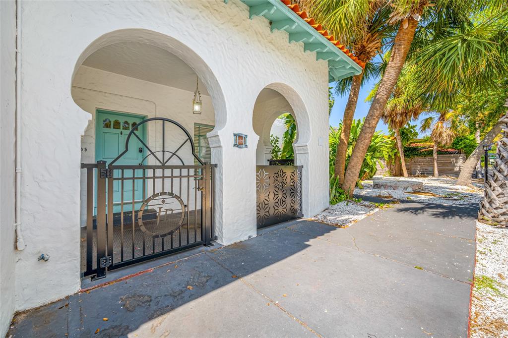 A white stucco building features arched entryways, a black metal gate, and a turquoise door — 1700 PARK STREET N UNIT 105, ST PETERSBURG, FL