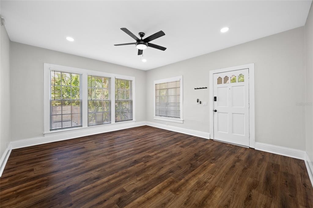 A living room features wood-look flooring, a ceiling fan, and a white front door — 1700 PARK STREET N UNIT 105, ST PETERSBURG, FL
