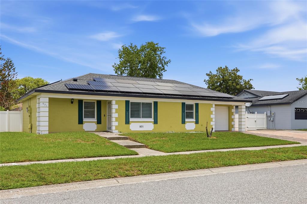 A single-story house with a yellow exterior, dark shutters, and solar panels on the roof — 931 ARIZONA WOODS LANE, ORLANDO, FL