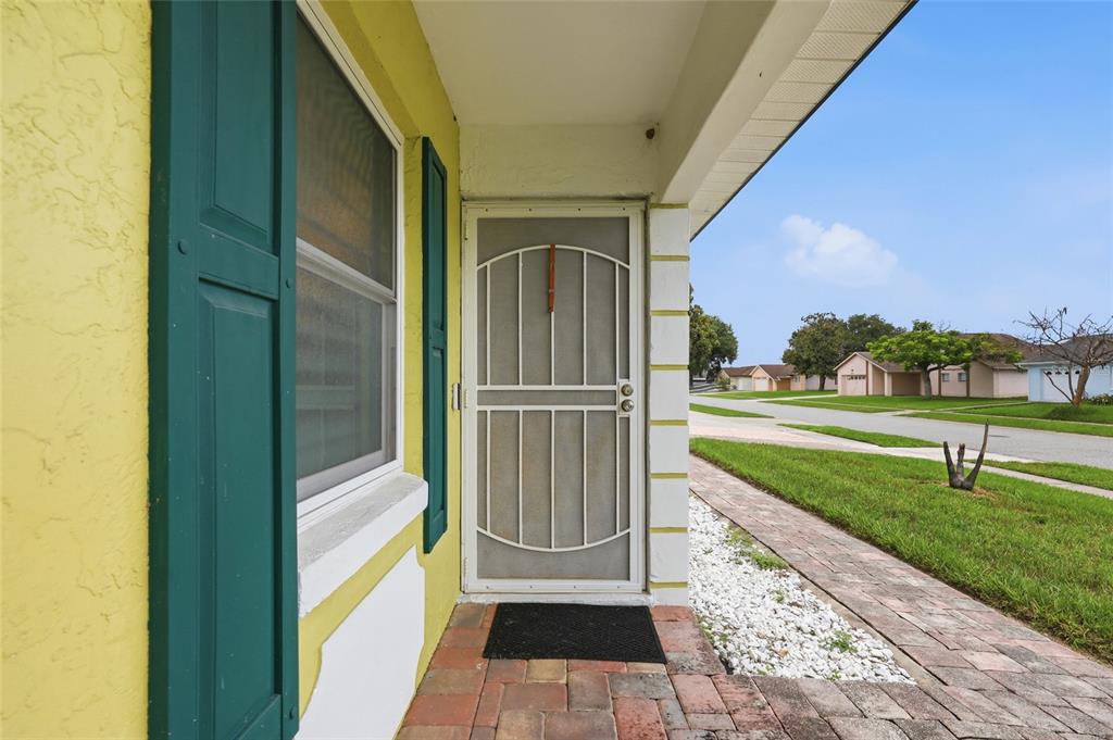 A yellow house exterior features a screen door, green shutters, and a brick walkway — 931 ARIZONA WOODS LANE, ORLANDO, FL
