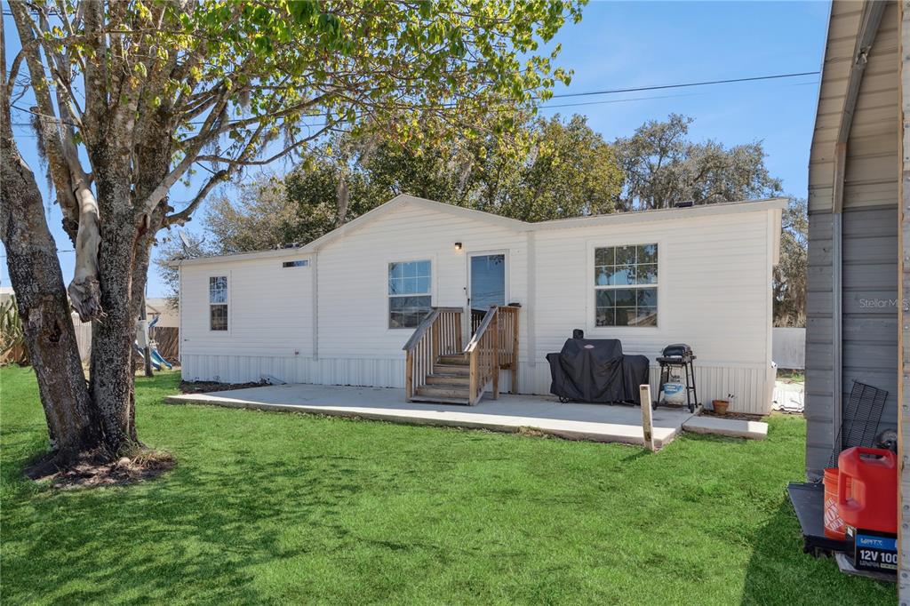 A white mobile home features a wooden staircase leading to a door above a concrete patio — 151 WILD FLOWER DRIVE, LAKE WALES, FL