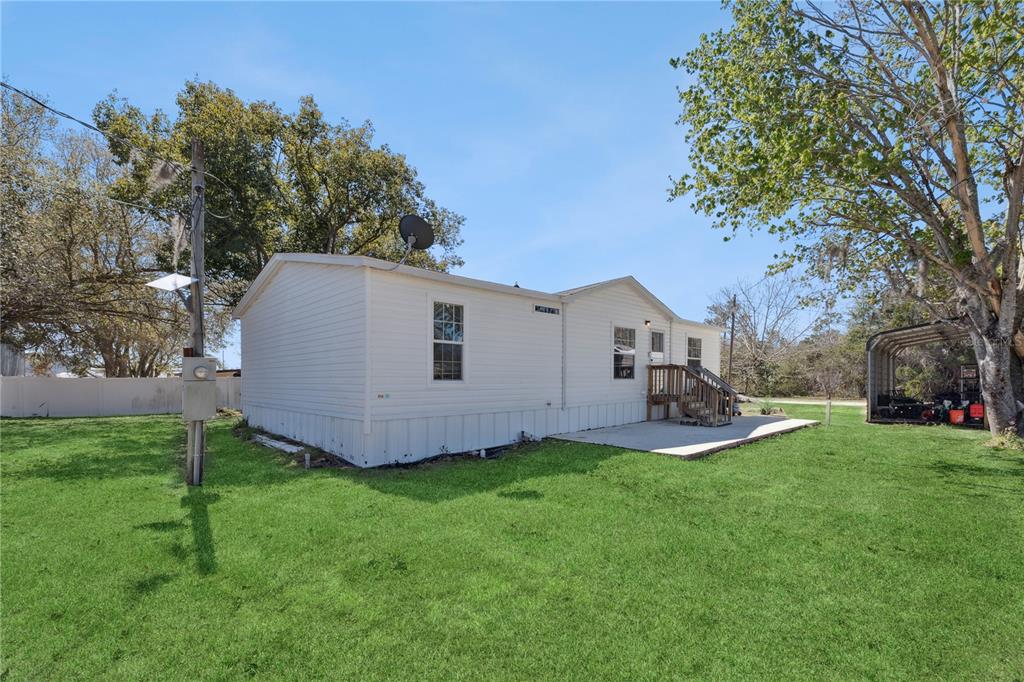 A white manufactured home sits on a grassy lot with a concrete patio and carport — 151 WILD FLOWER DRIVE, LAKE WALES, FL