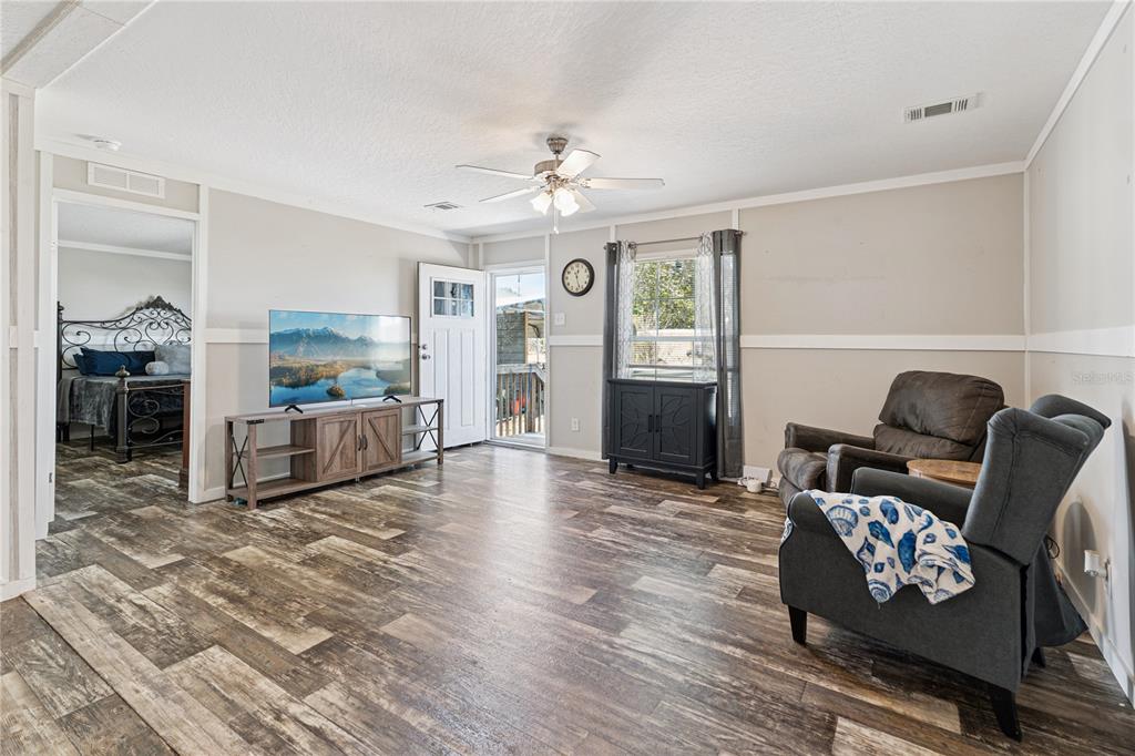 A living room features wood-look flooring, a ceiling fan, a television, and two armchairs — 151 WILD FLOWER DRIVE, LAKE WALES, FL