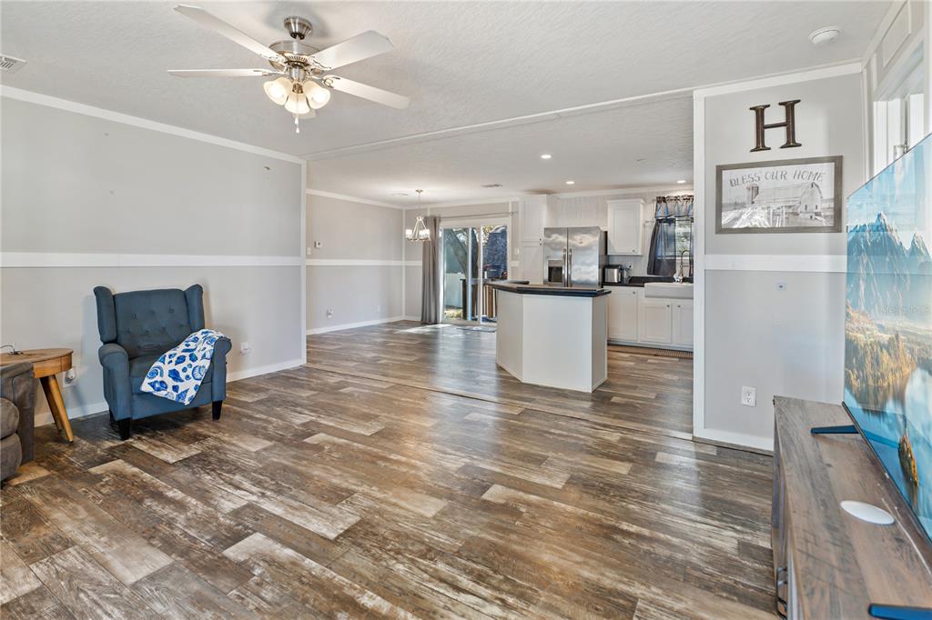 A living room with wood-look flooring flows into an open kitchen with white cabinetry — 151 WILD FLOWER DRIVE, LAKE WALES, FL