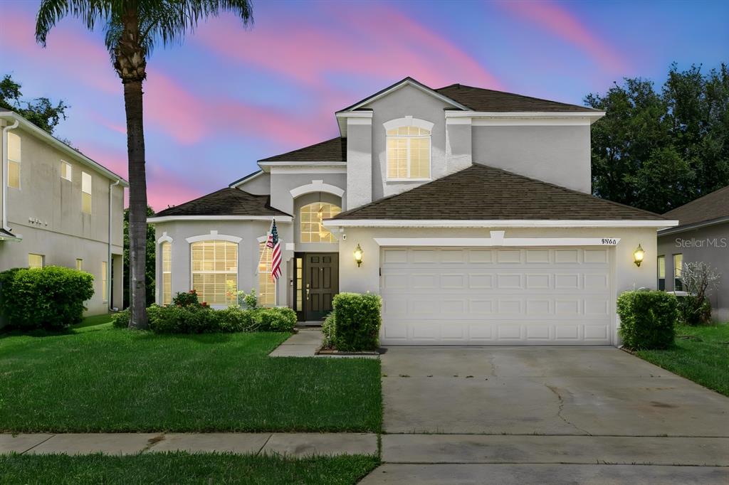 A two-story suburban house with a two-car garage and a palm tree in the yard — 9966 HIDDEN DUNES LANE, ORLANDO, FL