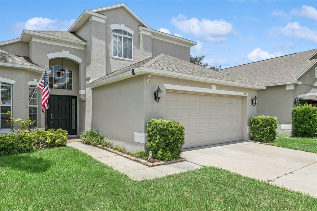 A two-story suburban house with a beige stucco exterior, a garage, and an American flag — 9966 HIDDEN DUNES LANE, ORLANDO, FL