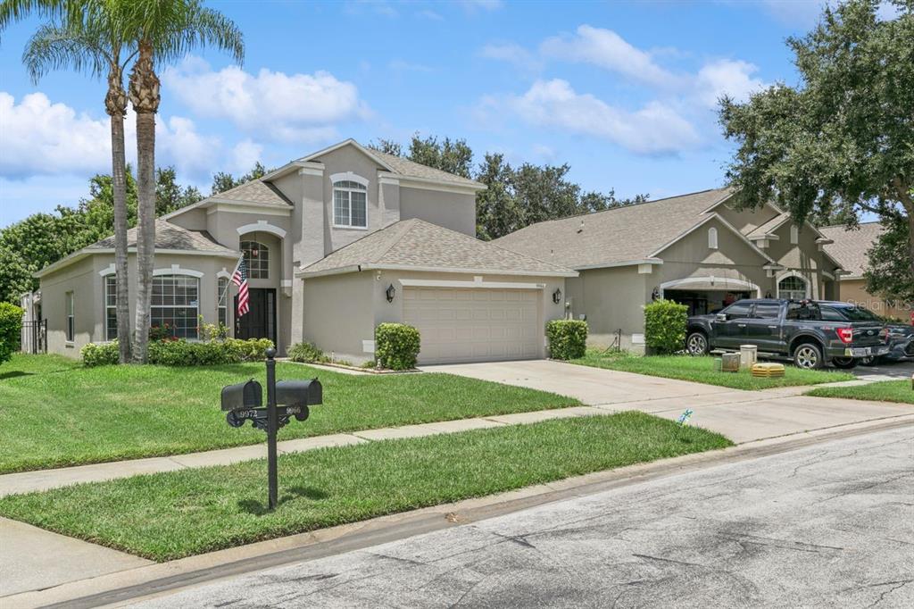 A two-story suburban house with a beige stucco exterior, a two-car garage, and palm trees — 9966 HIDDEN DUNES LANE, ORLANDO, FL