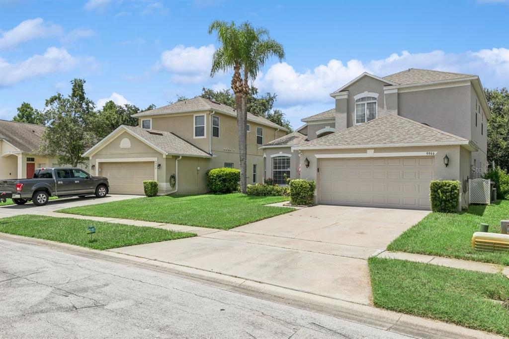 Two two-story suburban houses with attached garages and driveways under a blue sky — 9966 HIDDEN DUNES LANE, ORLANDO, FL