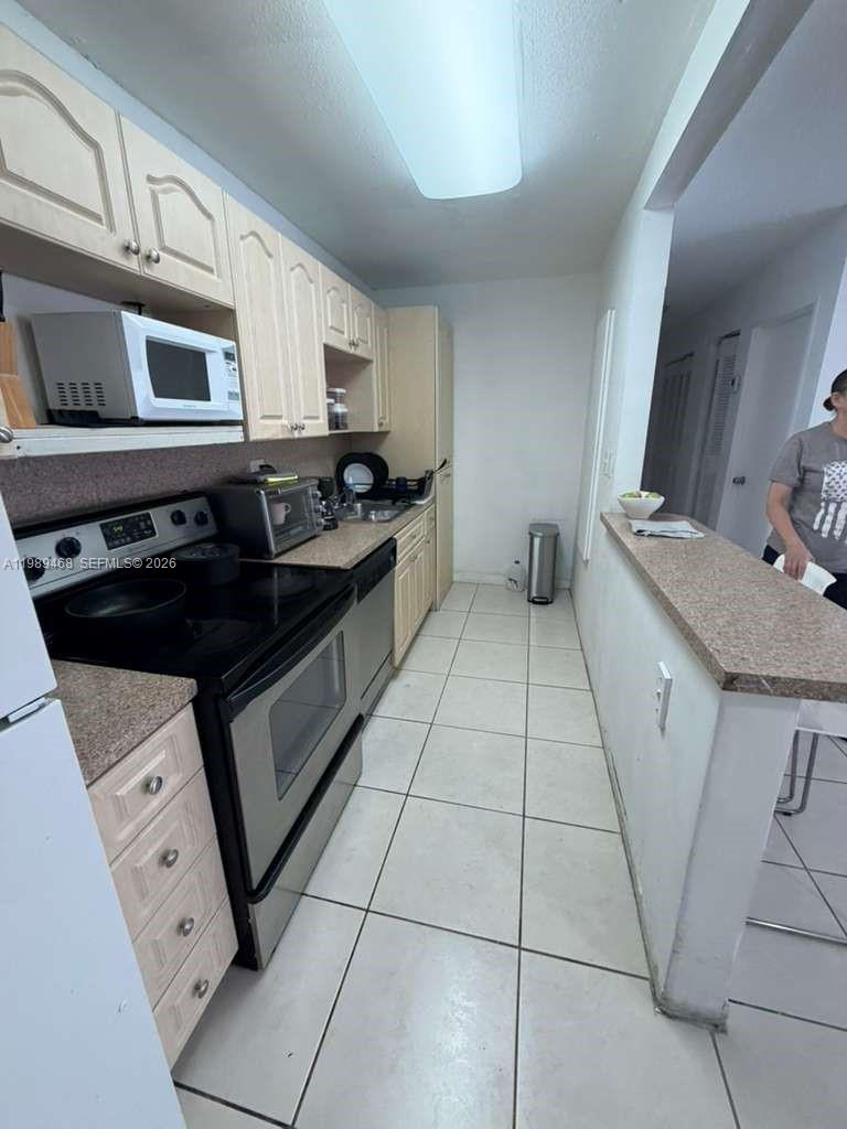 This galley kitchen features light wood cabinets, stainless steel appliances, and beige tile flooring — 4154 NW 79th Ave # 2A, Doral FL 33166, DORAL, FL