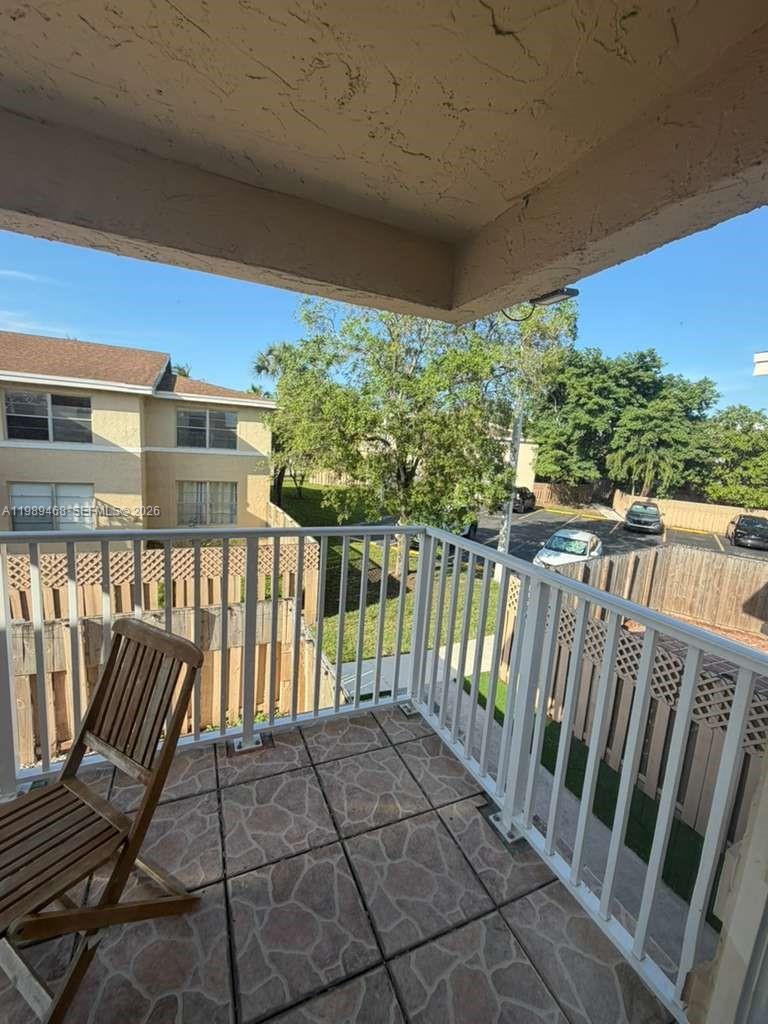 A balcony with tiled flooring, a wooden chair, and a white metal railing — 4154 NW 79th Ave # 2A, Doral FL 33166, DORAL, FL