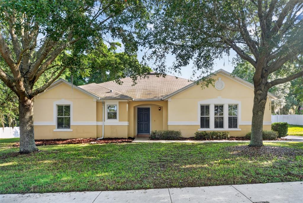 A single-story, yellow-stucco house with a dark blue front door sits behind two large trees — 2832 BREEZY MEADOW ROAD, APOPKA, FL