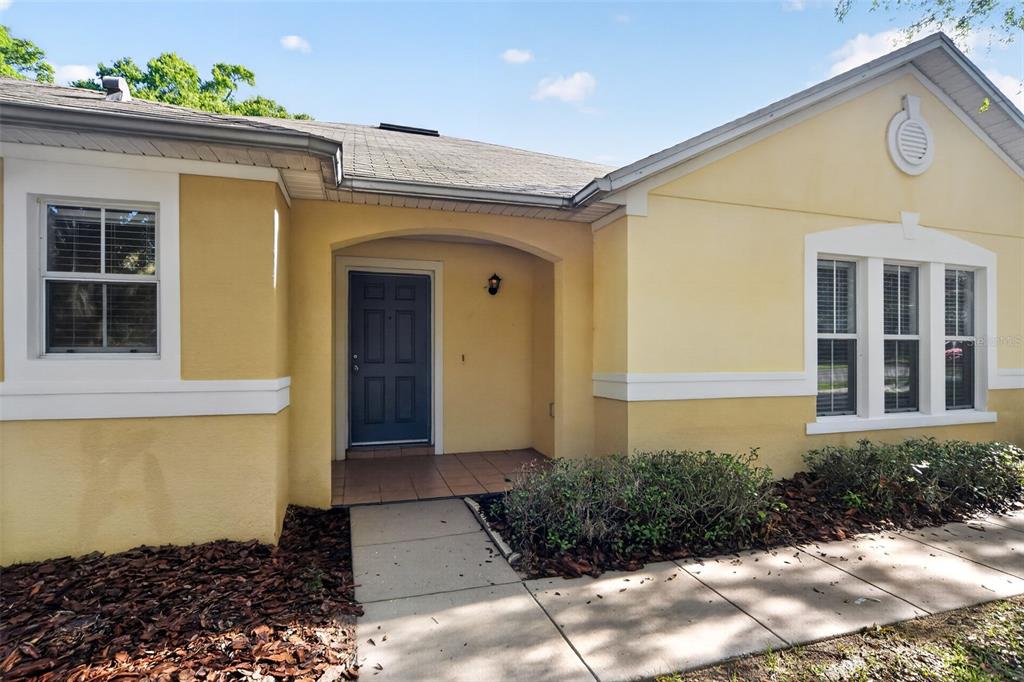 A yellow house exterior features a recessed entryway with a dark blue front door — 2832 BREEZY MEADOW ROAD, APOPKA, FL