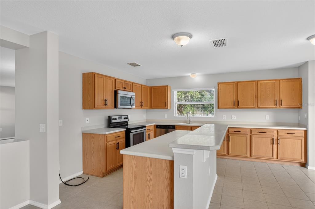 A kitchen with light wood cabinets, white countertops, a central island, and tile flooring — 2832 BREEZY MEADOW ROAD, APOPKA, FL