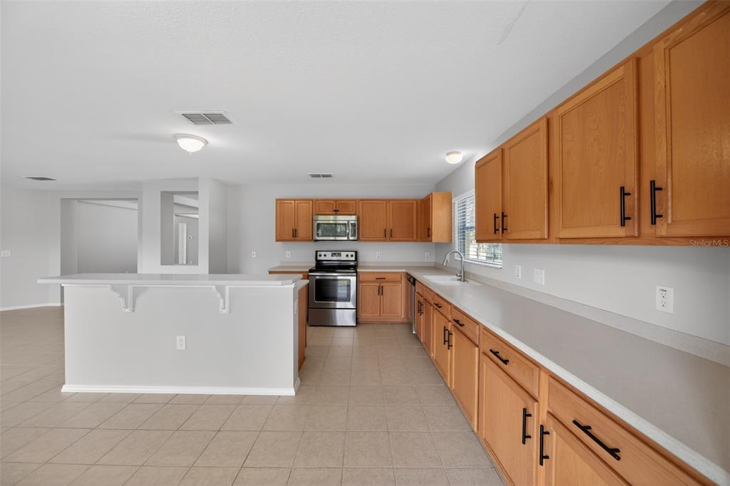 A kitchen features light wood cabinets, stainless steel appliances, and a breakfast bar island — 2832 BREEZY MEADOW ROAD, APOPKA, FL