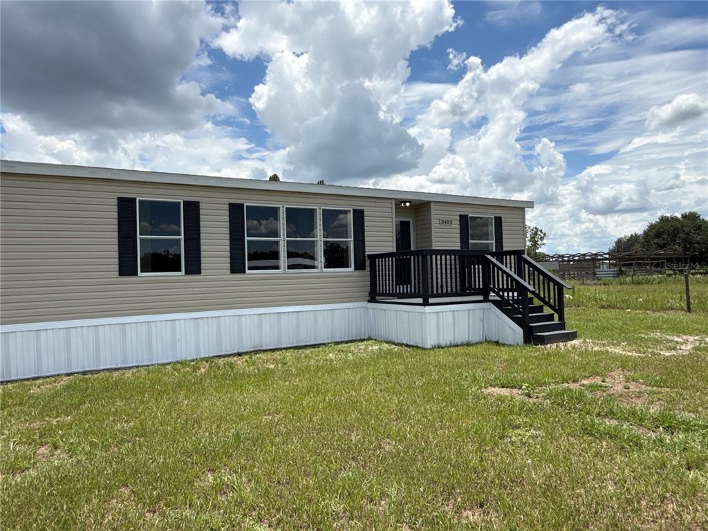 A tan manufactured home features a black wooden deck and stairs under a cloudy sky — 3483 BROOKE SMITH ROAD, FORT MEADE, FL