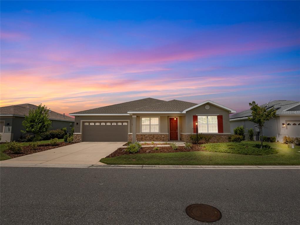 A single-story suburban house with a two-car garage and a landscaped front yard at sunset — 9070 SW 106TH AVENUE, OCALA, FL