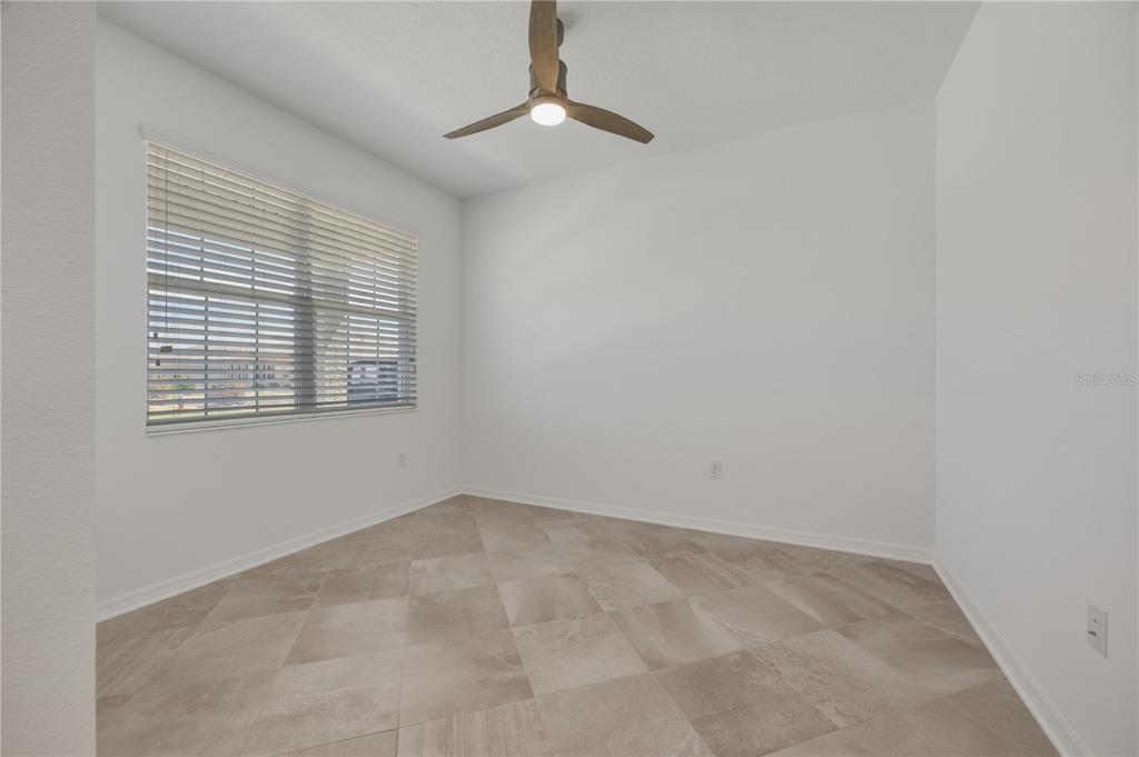 An empty room features white walls, a ceiling fan, and light-colored tile flooring — 9070 SW 106TH AVENUE, OCALA, FL