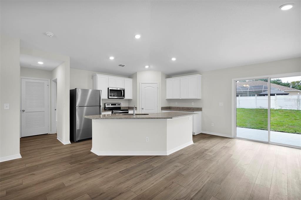 A kitchen with white cabinets, granite countertops, stainless steel appliances, and wood-look flooring — 2 RYMSHAW PLACE, PALM COAST, FL