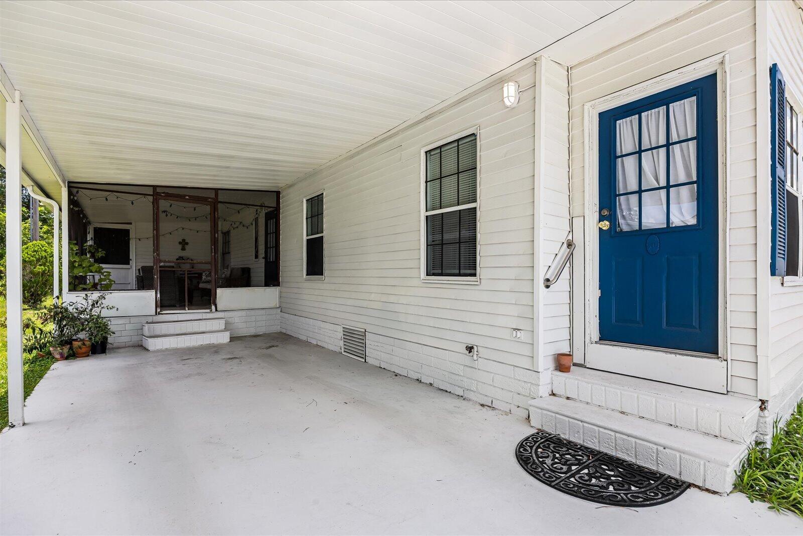 A white house exterior features a covered carport, a blue door, and a screened-in porch — 202 Sandy Bottom Place # 09, Fort Pierce FL 34982, FORT PIERCE, FL