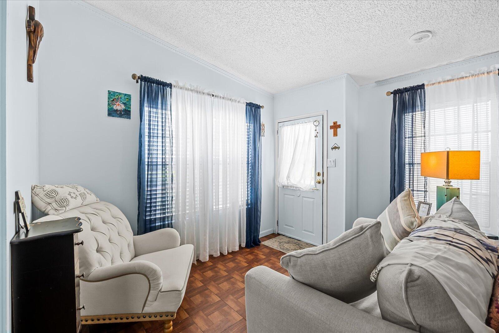 A living room features light blue walls, parquet wood flooring, a white armchair, and sofa — 202 Sandy Bottom Place # 09, Fort Pierce FL 34982, FORT PIERCE, FL