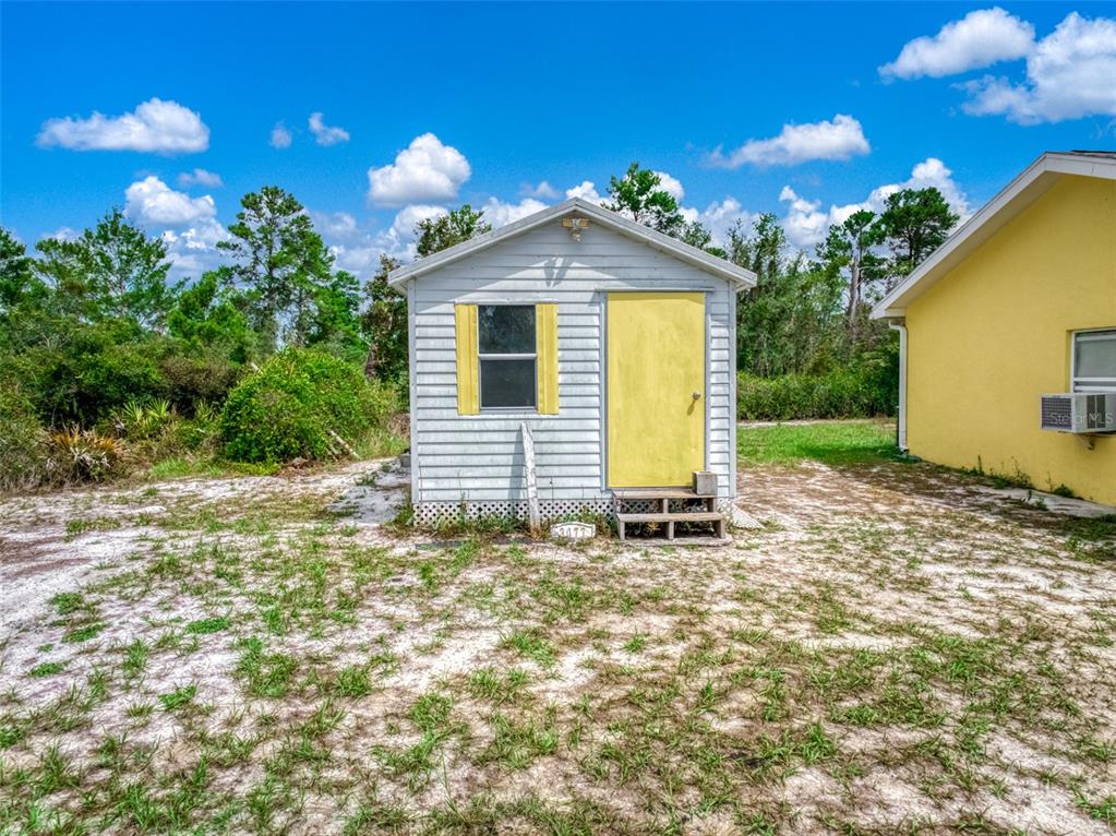 A small, white, single-story shed with a yellow door stands on a sandy lot — 3077 W SCORALICK ROAD, AVON PARK, FL
