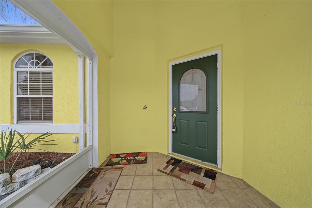 A yellow exterior entryway features a green front door, tiled flooring, and a window — 3077 W SCORALICK ROAD, AVON PARK, FL