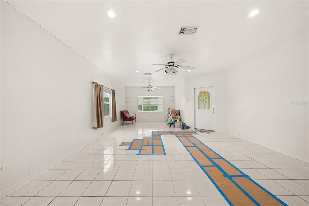 A bright, empty living room features white tile flooring with blue painter's tape markings — 3077 W SCORALICK ROAD, AVON PARK, FL