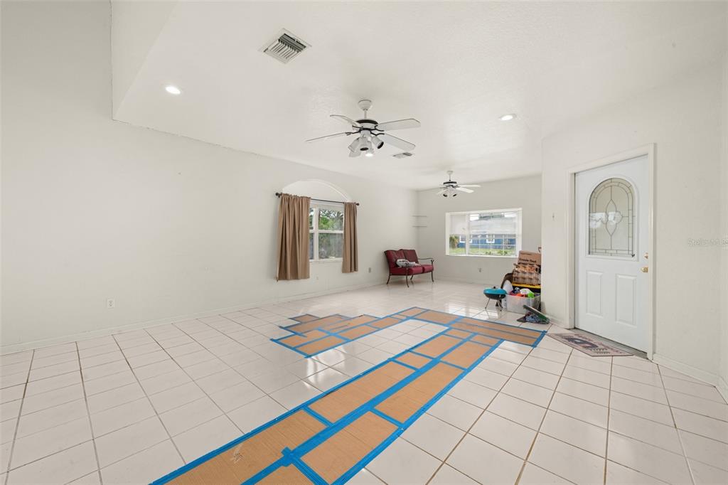 A bright living room features white tile flooring, vaulted ceilings, ceiling fans, and a front door — 3077 W SCORALICK ROAD, AVON PARK, FL