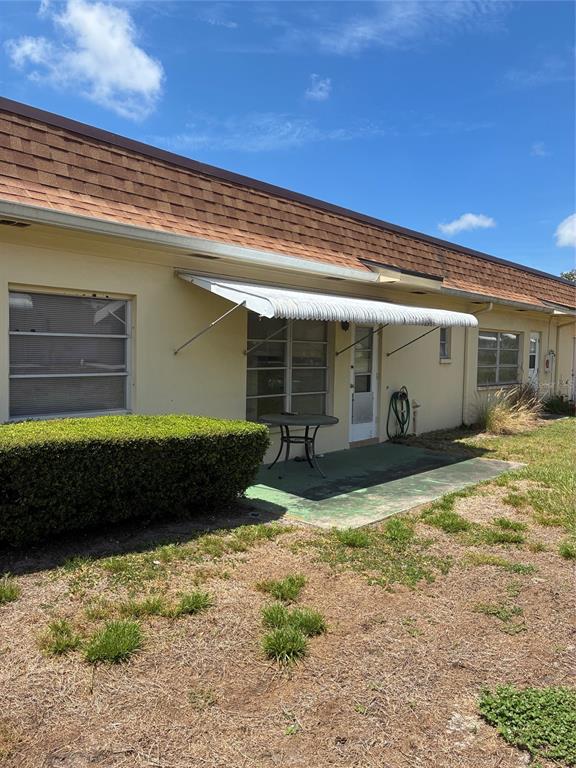 The exterior of a single-story building features a concrete patio, metal awning, and landscaping — 1657 S LAKE AVENUE UNIT 1, CLEARWATER, FL