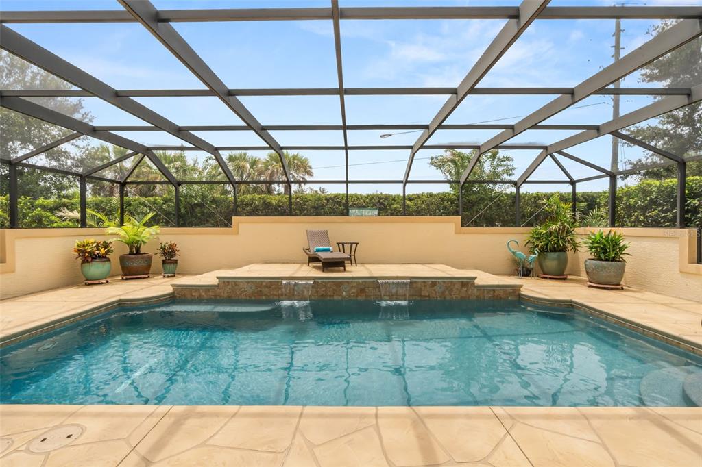 A swimming pool with two water features sits inside a screened-in lanai with potted plants — 2643 JUPITER WAY, THE VILLAGES, FL