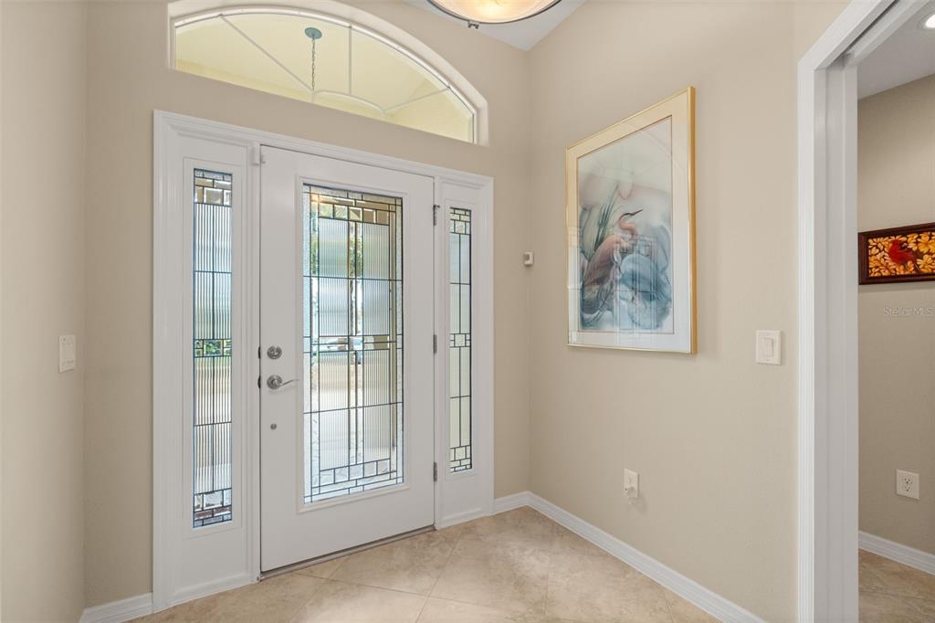 An entryway features a white front door with glass sidelights, tile flooring, and wall art — 2643 JUPITER WAY, THE VILLAGES, FL
